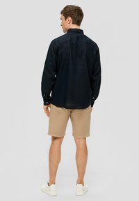 Donkerblauwe langarmshirt van katoenmix, met knoopmanchetten, gecombineerd met beige shorts en witte sneakers. Model gezien van achter.
