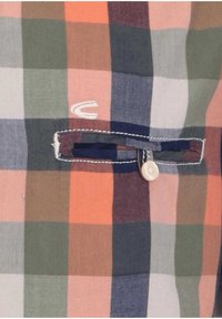 Tela de tartán multicolor con un bolsillo horizontal abotonado que presenta costuras blancas y un pequeño logotipo bordado en blanco cerca del bolsillo.
