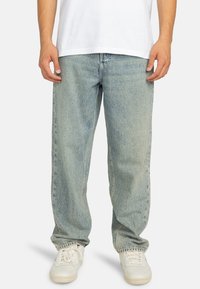 Lichtblauwe, casual jeans met een vervaagde textuur en rechte pijpen, gecombineerd met witte sneakers en een eenvoudig wit t-shirt.