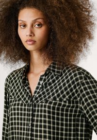 Camicia di flanella a scacchi bianca e nera con colletto sbottonato e tasca sul petto, caratterizzata da una morbida texture e una vestibilità ampia.