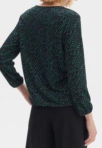 Blusa nera con un motivo astratto verde, maniche lunghe con polsini elasticizzati e scollatura rotonda. Tessuto leggero con una texture liscia.