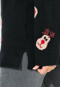 Schwarzer Strickpullover mit Rentiermotiven in Creme und Rot. Verfügt über seitliche Schlitze und gerippte Bündchen, die ein strukturiertes Gefühl bieten.