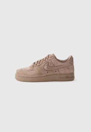Niskie beżowe zamszowe sneakersy Nike Air Force 1 z brązową gumową podeszwą i sznurowanym zapięciem na jasnym tle.