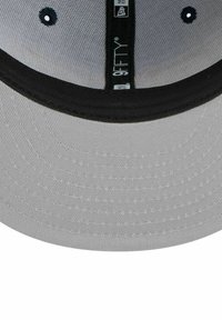 Casquette grise avec une visière noire, présentant une texture de tissu lisse. L'intérieur comprend des étiquettes, avec la marque '9FIFTY®' visible.