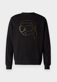 Felpa nera a maniche lunghe con una grafica di arte lineare dorata raffigurante un volto che indossa occhiali da sole grandi e una coda di cavallo al centro davanti.