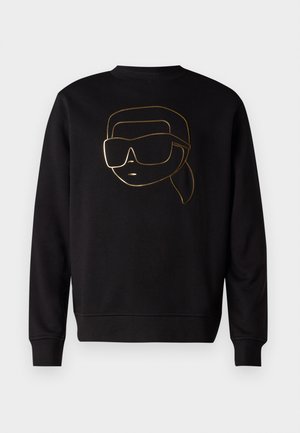Čierna mikina s dlhým rukávom, na prednej strane so zlatou kresbou tváre s veľkými slnečnými okuliarmi a copom.