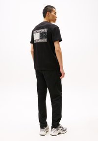 Camiseta de algodón negra con un gráfico rectangular impreso en la parte posterior, que presenta una mezcla de patrones, combinada con pantalones negros y zapatillas.