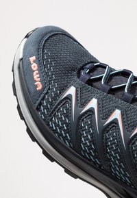 Zwarte en blauwe sportschoen met een bovenwerk van mesh, roze logo en unieke hoekige accenten. Heeft een dikke zool en een gestructureerd oppervlak voor grip.