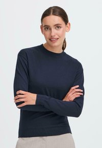 Granatowy sweter wykonany z miękkiego materiału, z okrągłym dekoltem, długimi rękawami i prążkowanymi mankietami. Prosty design z gładką teksturą.