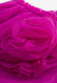 Tissu en tulle fuchsia disposé en plis doux et superposés avec des bords froncés, mettant en valeur une texture translucide et une couleur vive.