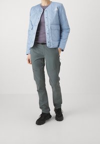 Jasnoniebieska pikowana kurtka na zatrzaski, noszona na ciemnofioletowej bluzce, w połączeniu z ciemnoszarymi spodniami i czarnymi butami trekkingowymi.