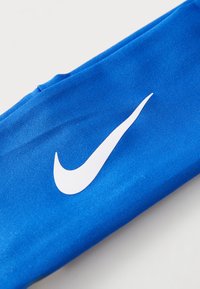 Plavi čelenka od tkanine s teksturiranim završetkom, s istaknutim bijelim Nike swoosh logotipom sa strane.