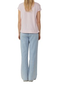Lichtroze shirt met korte mouwen en een ontspannen pasvorm, gecombineerd met brede lichtblauwe spijkerbroeken, wat zorgt voor een casual, losse look.