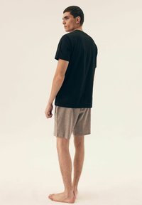 Czarny bawełniany t-shirt i szare szorty w luźnym kroju. Model stoi boso i jest widoczny z tyłu na neutralnym tle.