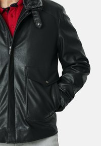 Chaqueta de cuero negra con un cuello de piel gris, cierre frontal con cremallera, dos grandes bolsillos con tapa y acabado texturizado.