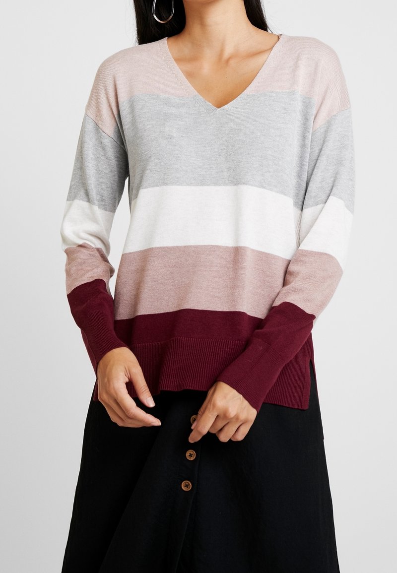 Pull à col en V à manches longues présentant des rayures horizontales en gris clair, blanc, mauve et bordeaux. Poignets côtelés et fentes sur les côtés.