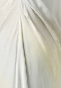 Lätt, flödande tyg i mjukt vitt med subtil lyster. Har draperade veck och slät textur, vilket skapar mjuka vågor och djup.