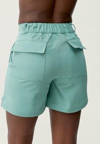 Lichtgroene cargoshorts met een taillekoord, voorzien van twee achterzakken en zijsplitten. De stof lijkt glad en lichtgewicht te zijn.