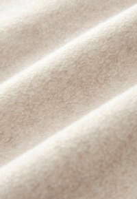 Tela de color beige claro con una superficie suave y texturada que presenta fibras y pliegues sutiles, indicando un material mullido y acogedor.