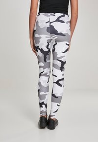 Magas derekú leggings fekete, szürke és fehér álcafóliával, szoros illeszkedéssel és sima textúrával, fekete sportcipővel párosítva.