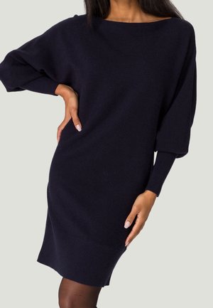Robe tricotée bleu marine, avec une coupe ample, un décolleté bateau large et des manches longues. Présente une texture côtelée et un ourlet, offrant un aspect confortable.