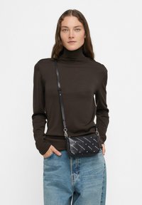 Czarna torebka typu crossbody o teksturowanej powierzchni, z powtarzającym się białym wzorem logo, srebrnym okuciem i regulowanym paskiem.