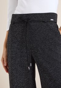 Pantaloni jogger neri con motivo a maglia testurizzato, dotati di vita regolabile con coulisse e dettagli metallici. Design casual e vestibilità rilassata.