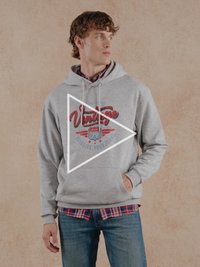 Grijze hoodie met een vintage rood logo, voorzien van een trekkoord en een voorzak, gedragen over een geruit overhemd en een blauwe spijkerbroek.