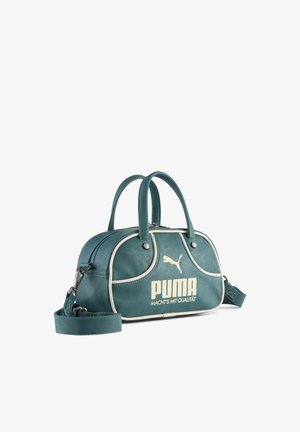 Turkio spalvos Puma rankinė su dviem rankenomis, nuimamu petnešos dirželiu, kreminės spalvos apdaila, Puma logotipu ir priekyje esančiu užrašu „MACHT’S MIT QUALITÄT“.