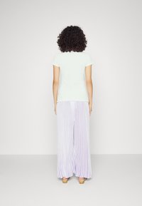 Vaaleanvihreä lyhythihainen paita yhdistettynä pitkään, pleatattuun laventelinväriseen ja valkoiseen raidalliseen housupukuun. Asu on yksinkertainen ja rento.