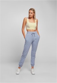 Lys gul kort tanktop med firkantet hals, kombinert med blå joggebukser med snøring i midjen og ankelmansjetter, båret med hvite sneakers.