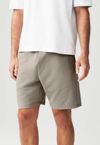 Shorts grises hechos de una tela lisa y ligera, con un corte recto, bolsillos laterales y una cinturilla elástica. Llevados con una camiseta blanca.
