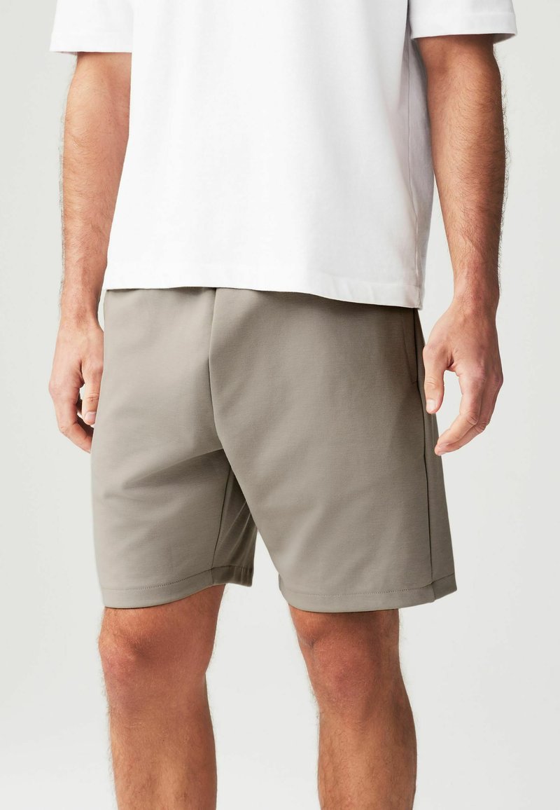 Pantaloni corto grigi realizzati in tessuto leggero e liscio, con una linea dritta, tasche laterali e una cintura elastica. Indossati con una maglietta bianca.