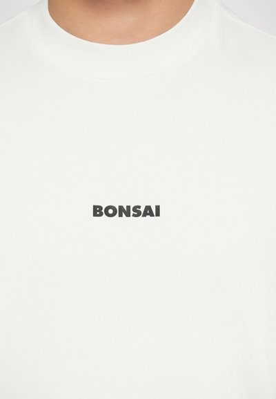 T-shirt bianca in cotone con una stampa grafica nera "BONSAI" in un font audace centrata sul petto. Maniche corte e scollatura rotonda.