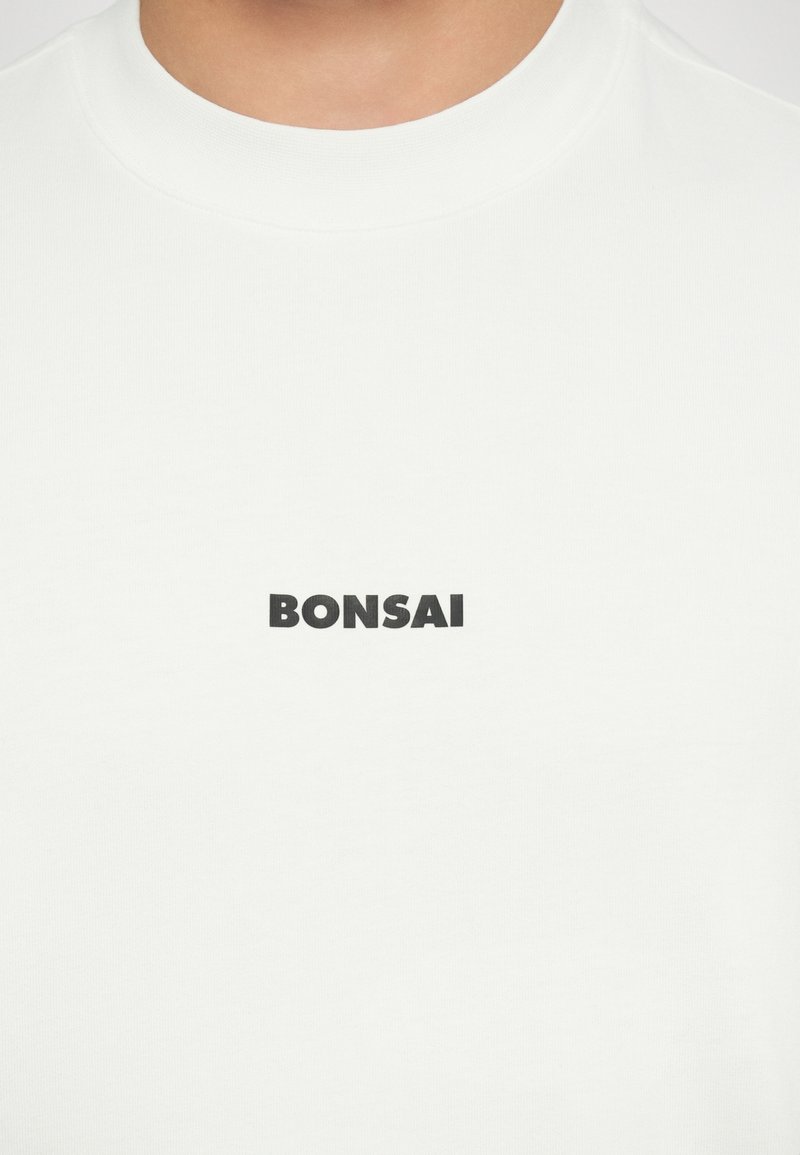 White cotton t-shirt featuring a black "BONSAI" graphic print in a bold font centered on the chest. Short sleeves and round neckline.