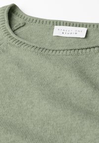 Hellgrüner Strickpullover mit rundem Halsausschnitt und feinen Rippdetails. Das Etikett trägt die Aufschrift "Street One Studio." Weicher, strukturierter Stoff.