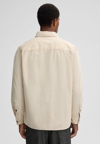 Beige corduroy shirt with a pointed collar, long sleeves, and buttoned cuffs; features vertical ribbed texture.