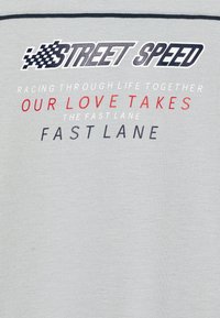 Camiseta de algodón gris con texto impreso en negro, rojo y gris, que incluye frases con temática de carreras. Diseño de cuello redondo y mangas cortas.