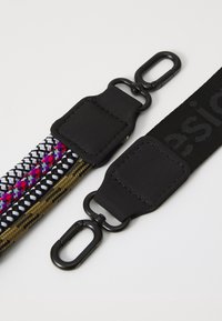 Punottu hihna, jossa musta, valkoinen ja violetti kuviointi ja musta lukko. Vieressä yhtenäinen musta hihna, jossa kohokuvioitu logo ja lukko.