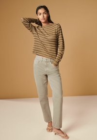 Haut à rayures marron à manches longues avec un col bateau, associé à un pantalon droit beige clair et des tongs à talons couleur tan sur un fond neutre.