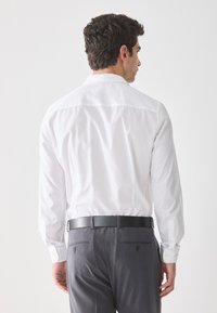 Witte overhemden met lange mouwen, zachte textuur en knoopmanchetten, gecombineerd met grijze broek met twee achterzakken en een slank zwart leren riem.