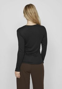 Zwarte langemouwshirt met een aansluitend ontwerp, ronde halslijn en een gladde textuur, gecombineerd met bruine wijde broek. Achteraanzicht.