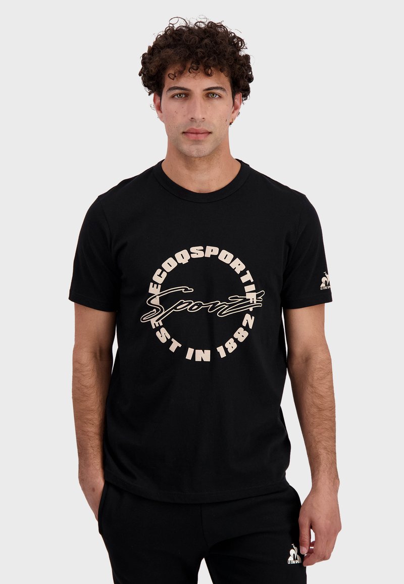 T-shirt en coton noir avec un graphique circulaire beige portant les inscriptions "ECOQSPORT" et "EST EN 1882". Manches courtes et design col rond.