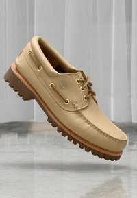 Beige Lederbootsschuh mit tanfarbener Gummisohle, Metallösen und genähten Details. Verfügt über ein kleines Logo an der Seite.