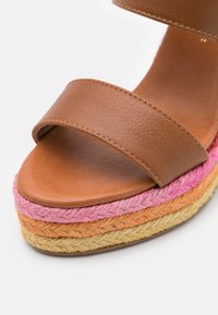 Sandalia de cuero marrón con dos correas anchas, que presenta una plataforma de cuerda trenzada multicolor en tonos rosa, naranja y beige.