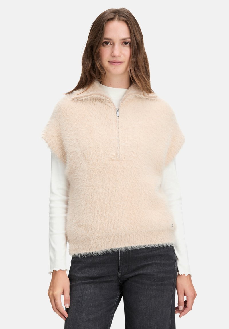 Lichtroze pluizige vest met een rits aan de voorkant en een gespleten kraag, gedragen over een wit shirt met lange mouwen, gecombineerd met donkere jeans.