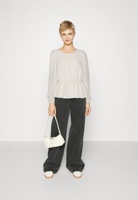 Light grey, long-sleeve peplum top with elastic waist, paired with high-waisted black wide-leg pants. Accessorized with a small white handbag.