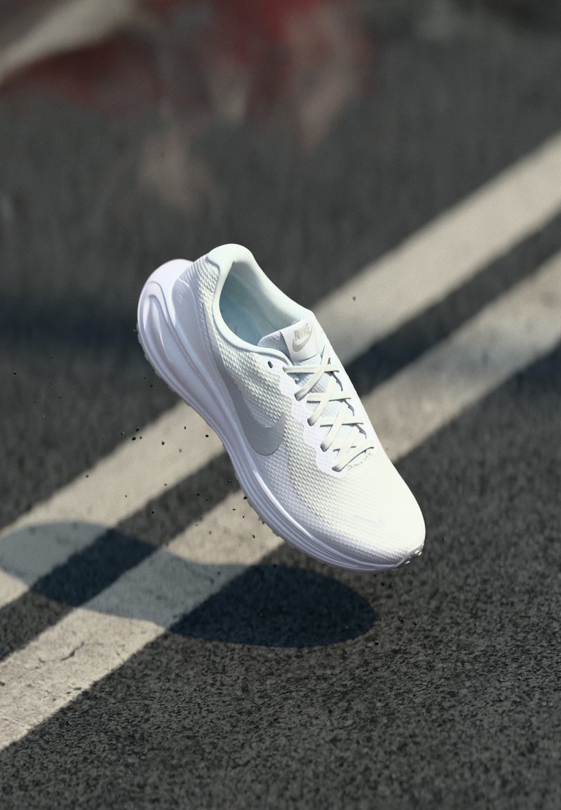 White lightweight running shoe with mesh upper, padded collar, and rubber sole. Features grey Nike logo and laces, suspended above pavement.