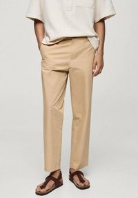 Bežna bombažna hlače s ravnim krojem, v kombinaciji s svetlo bež ohlapno srajco. Obuti so z rjavimi japonkami. Enostaven dizajn in sproščen kroj.