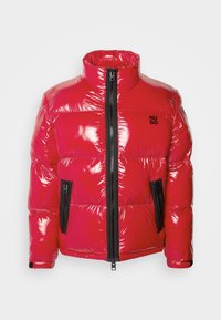Veste matelassée rouge brillante avec col montant, fermeture éclair centrale noire, deux poches zippées noires et petit logo noir "HUGO" sur la poitrine.